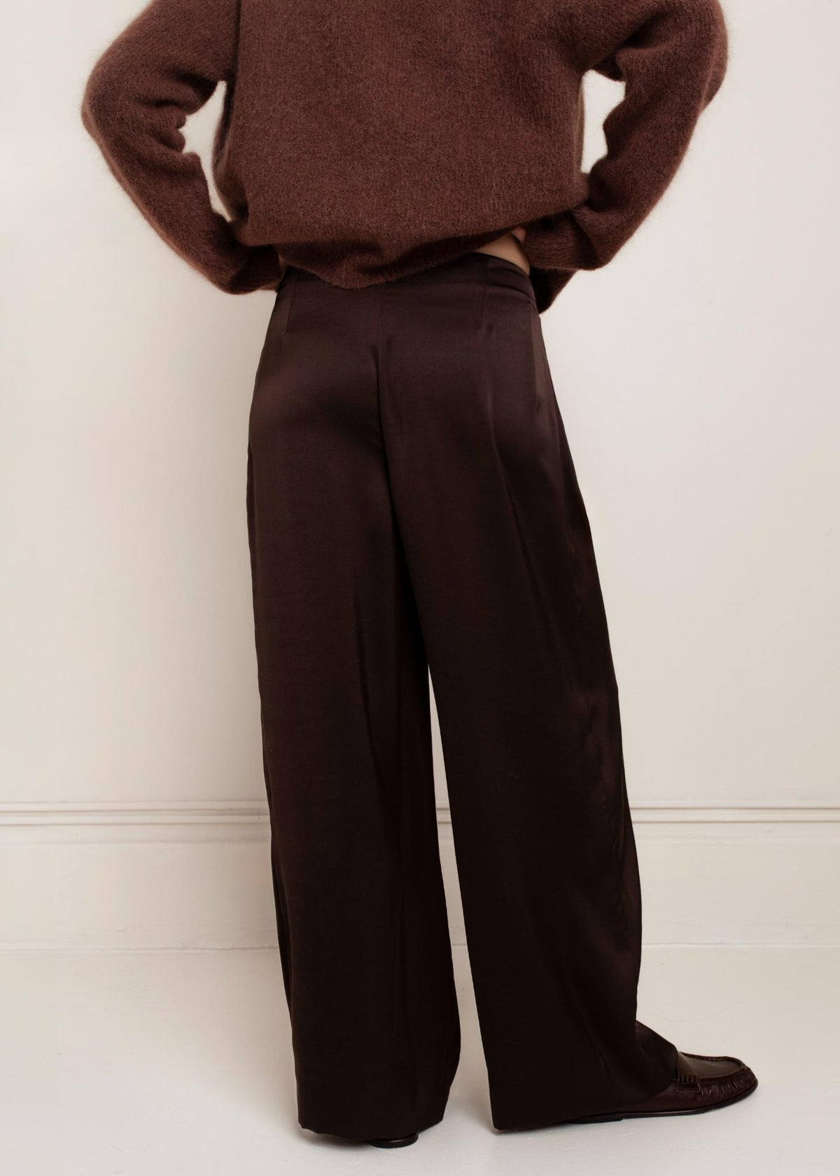Back view of wide-leg satin chocolate brown trousers styled with brown sweater and loafers